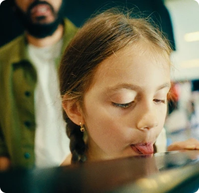 Criança com tranças encostando a língua em uma superfície de vidro.